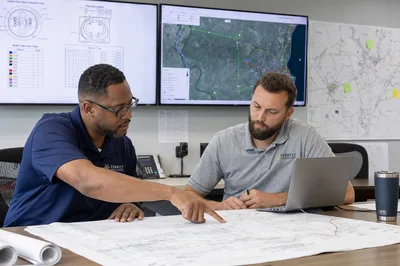 Project manager reviewing fiber network design deliverables on a laptop with outsourced engineering team on video call