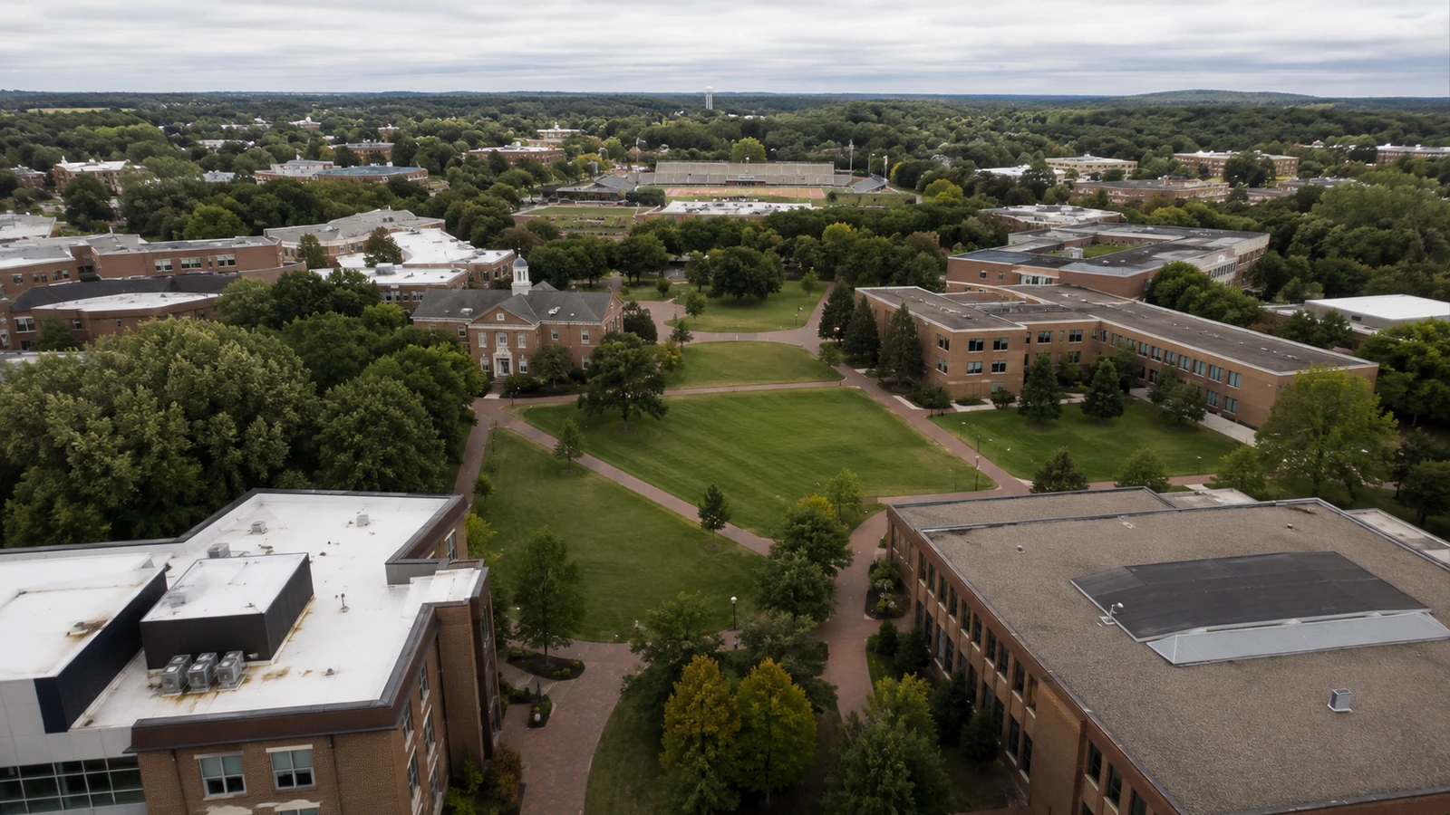 Oblique aerial view of a university campus with brick buildings, tree-lined walkways, and a stadium
