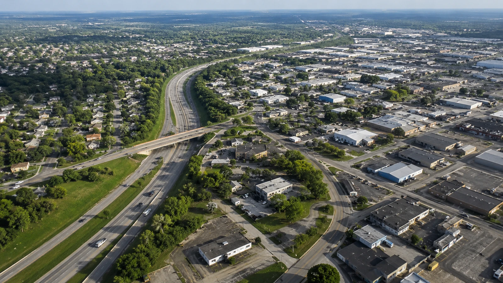Oblique aerial view of a divided highway, bridge, local streets, homes, and a light-industrial district