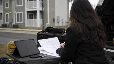 A person marks up floor-plan drawings on a truck tailgate outside a multi-unit apartment building.