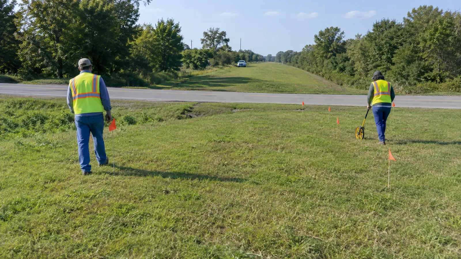 Two surveyors mark a proposed crossing across a maintained grass right-of-way.