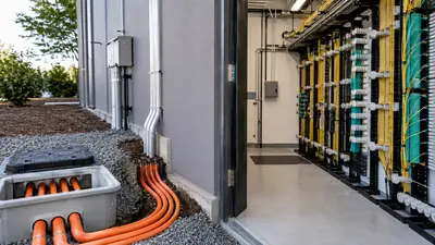 Outside conduit route entering a telecom facility beside indoor fiber distribution racks
