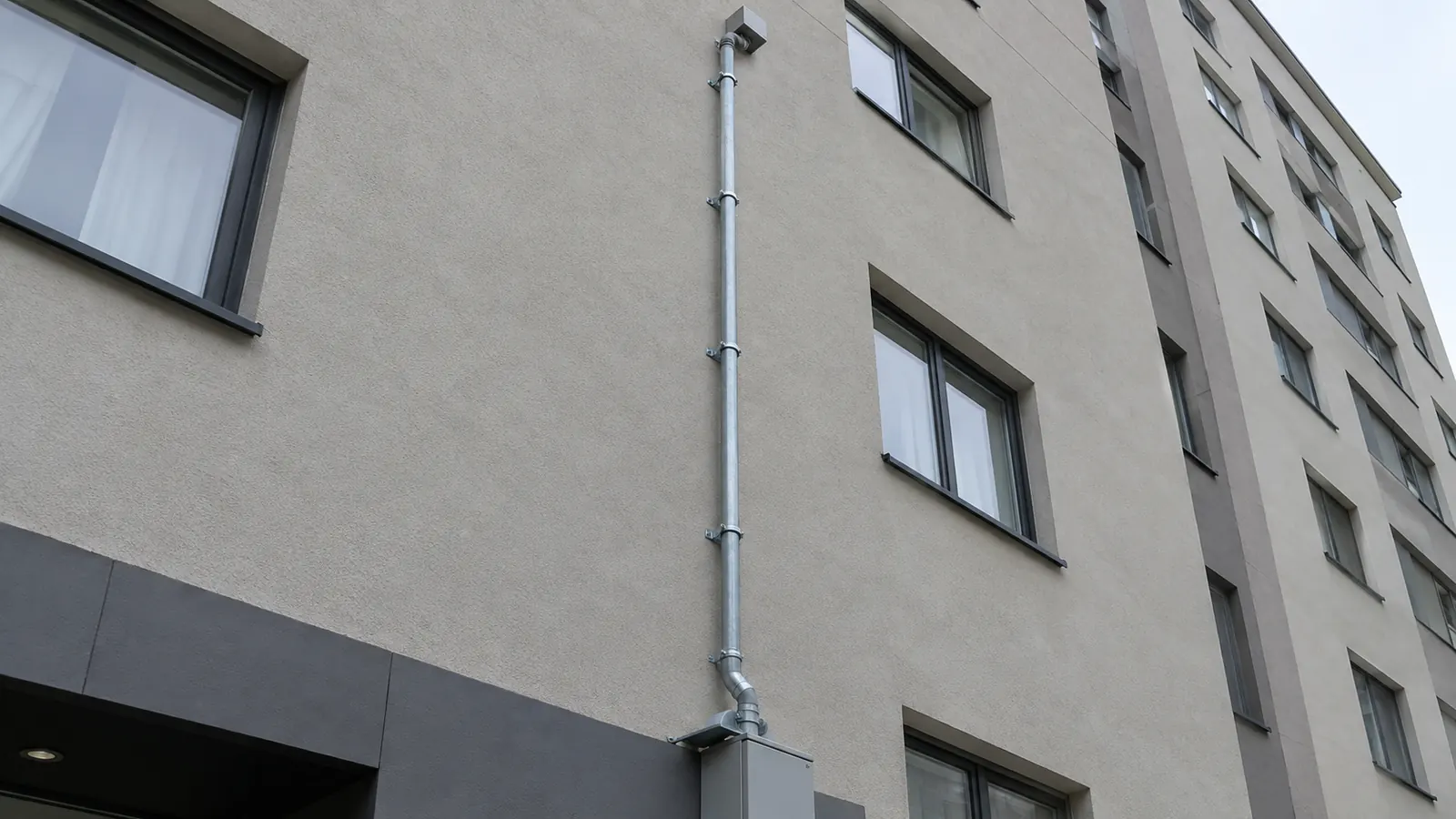 A secured vertical telecommunications conduit riser attached to the exterior wall of a multi-story building.
